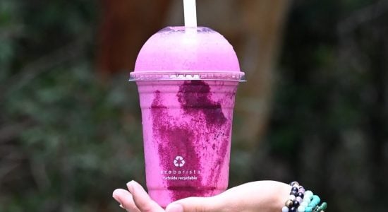 Hand balancing a pink smoothie in a recyclable cup from mobile juice trailer